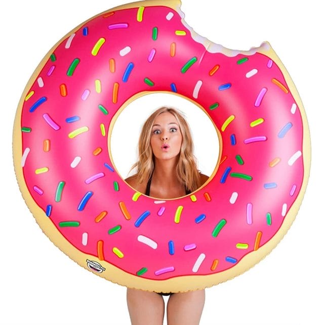 Image shows a giant doughnut shaped pool float fully inflated. A lady with blonde hair is holding the pool float aloft.