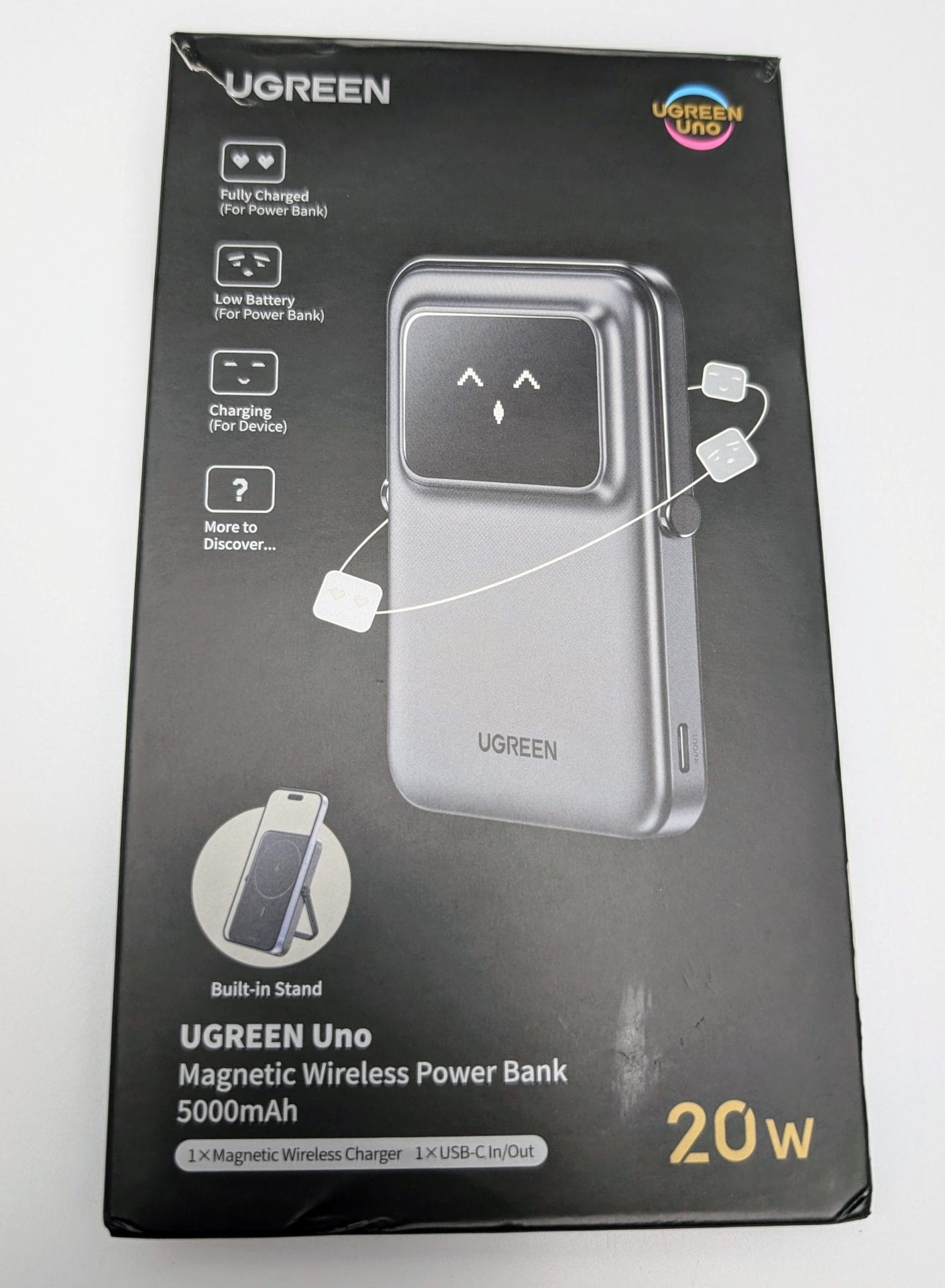 A black box for UGREEN Uno Magnetic Wireless Power Bank with a capacity of 5000mAh and 20W power. The front of the box shows the power bank with a digital display and two small square devices connected by a string. The display icons indicate battery status: fully charged, low battery, and charging. The text mentions features like a built-in stand, magnetic wireless charger, and USB-C input/output options. The UGREEN logo is at the top right corner of the box.