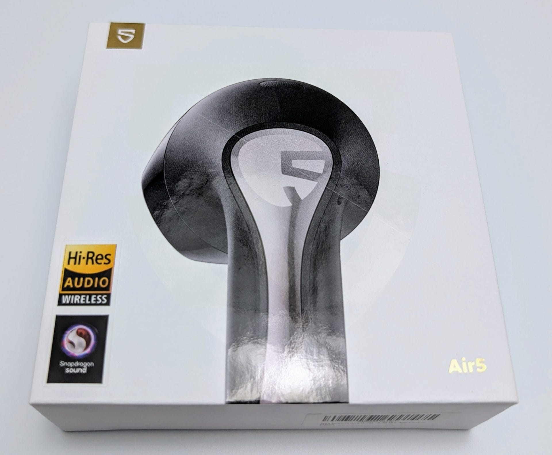 Image of a SoundPEATS Air5 Earbuds box. The box is predominantly white with a large image of a single black and silver earbud prominently displayed on the front. The earbud design features a sleek, modern look with a metallic finish. In the top left corner, there's a logo that reads 'S'. On the bottom right, the model name 'Air5' is printed in gold. The left side of the box has two badges: one for 'Hi-Res AUDIO WIRELESS' and another for 'Snapdragon sound'.