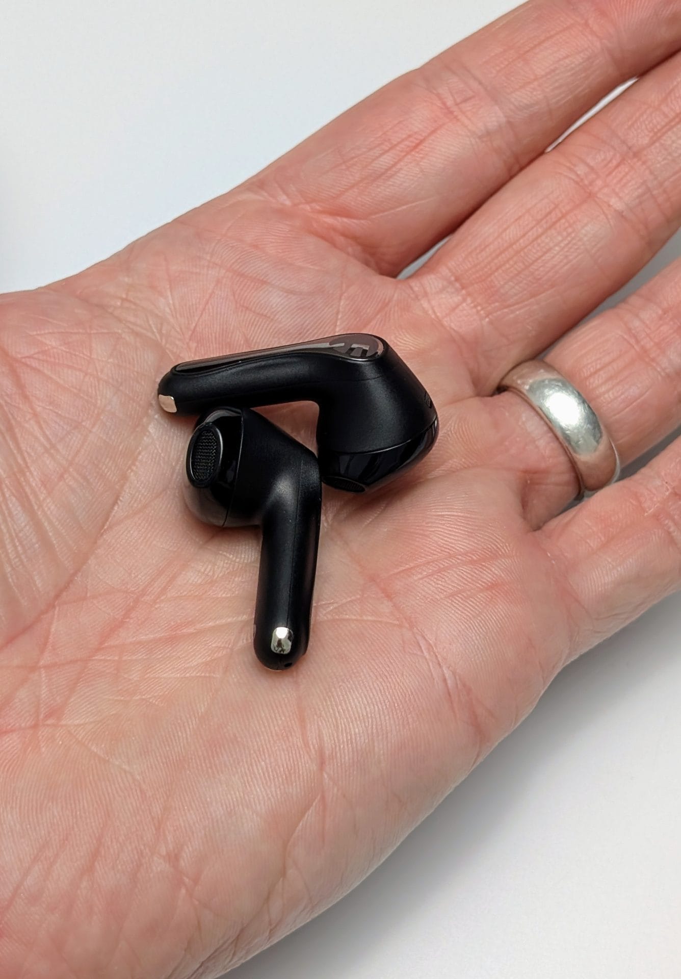 Image of a hand holding two SoundPEATS Air5 wireless earbuds. The earbuds are black with a sleek design, featuring a metallic accent on the top part. The hand is open, palm up, with the earbuds resting on it. The person wearing the hand also has a silver ring on their ring finger.