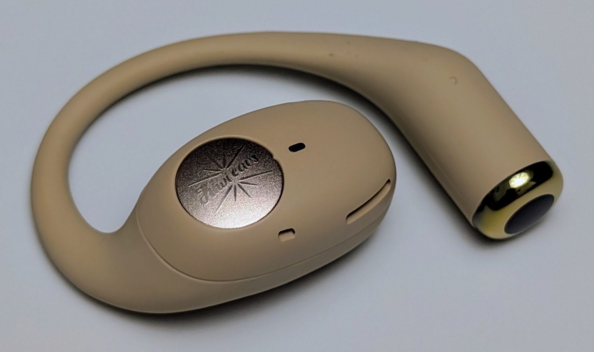 A single beige Kiwi Ears Spark earbud on a white background. The earbud has a hook design with a metallic silver circular piece featuring the "Kiwi ears" logo and a starburst design. The earbud body includes small ventilation holes, and the tip has a gold-colored ring around a black speaker opening.