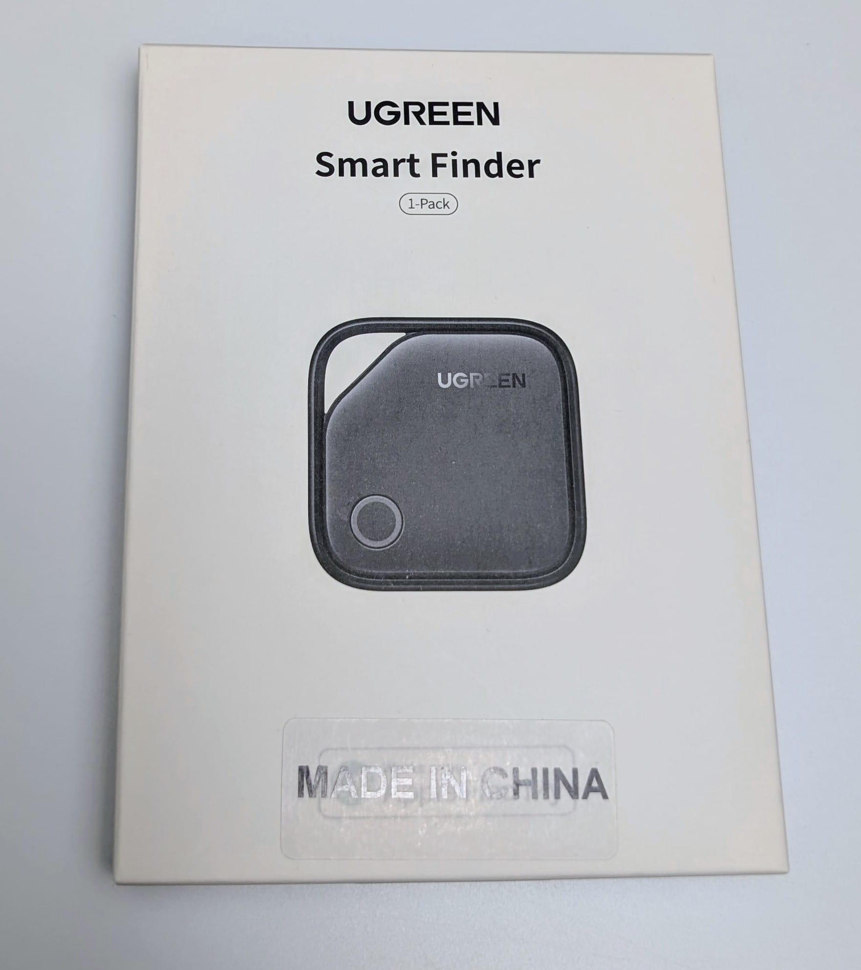 UGREEN FineTrack Smart Finder A white rectangular box with the text "UGREEN Smart Finder 1-Pack" at the top. Below the text is an image of a small, square, black UGREEN Smart Finder device with rounded corners, featuring the UGREEN logo and a circular button or sensor. At the bottom of the box, a label reads "MADE IN CHINA."