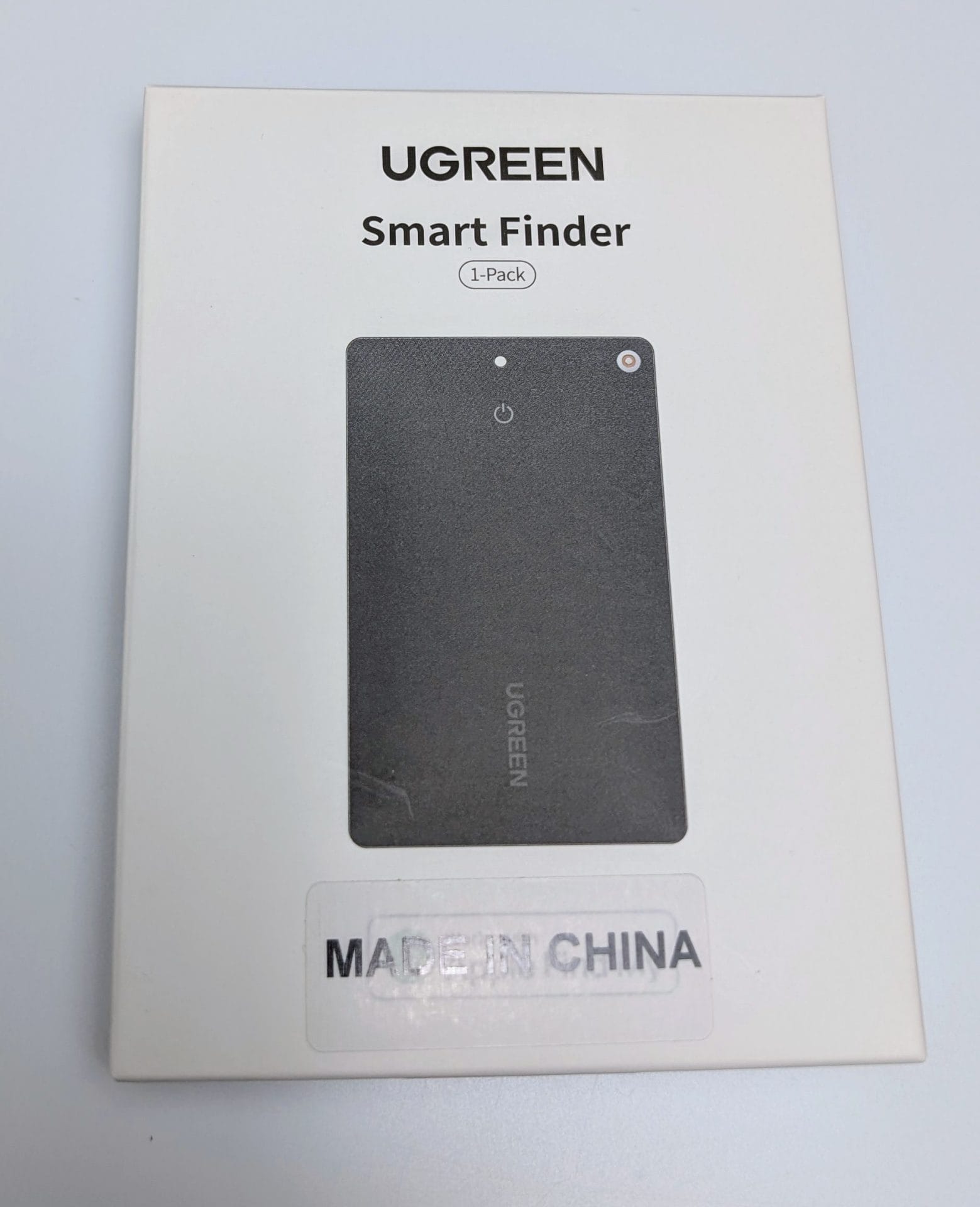 A white box with the UGREEN logo at the top, featuring an image of the FineTrack Slim Smart Finder, a thin, rectangular black device with a power button and a small hole in the top right corner. The text "Smart Finder" and "1-Pack" is printed below the logo. A "MADE IN CHINA" sticker is at the bottom.