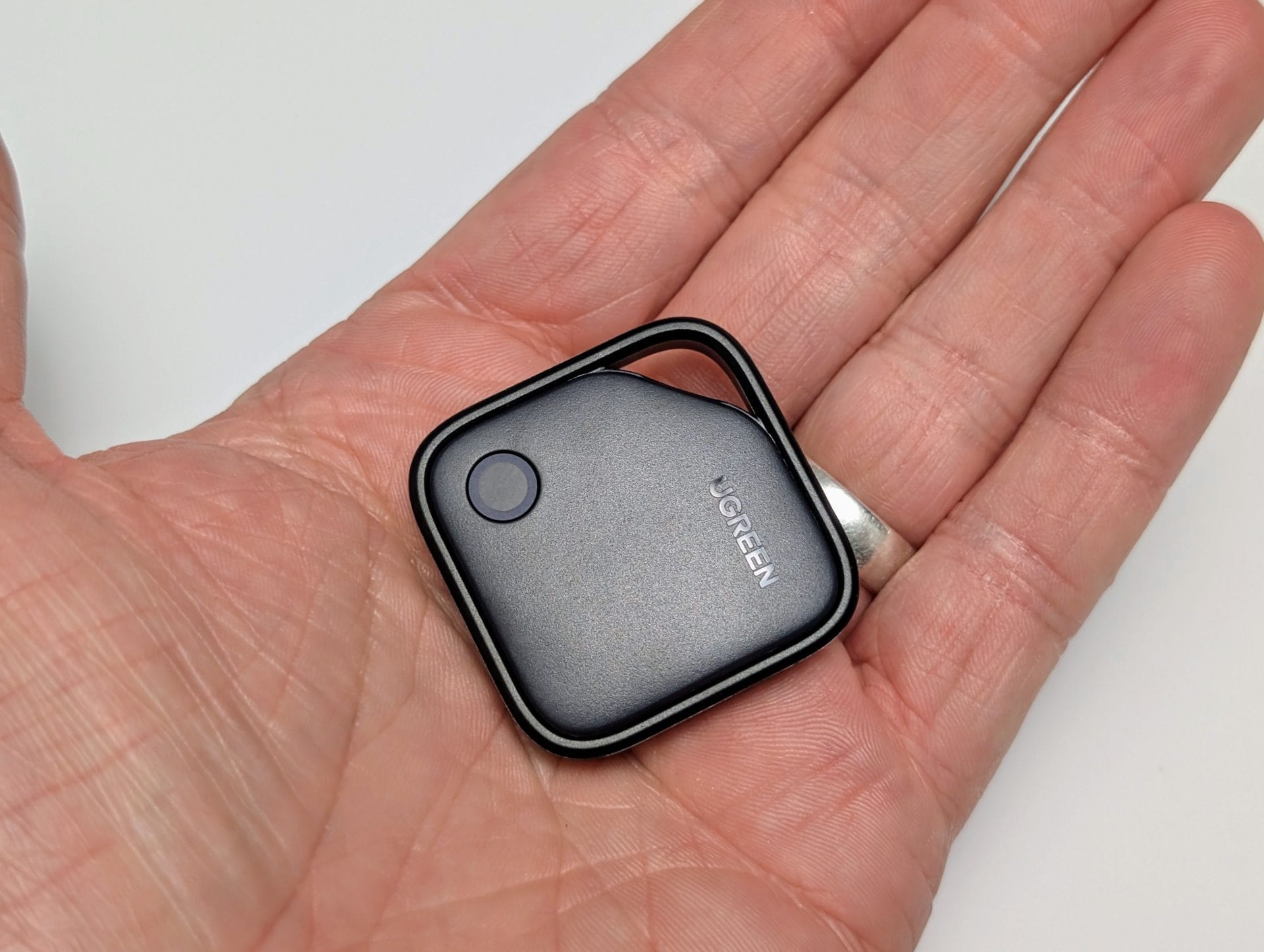 UGREEN FineTrack Smart Finder A hand holding a small, black UGREEN Smart Finder device with rounded corners. The device has the "UGREEN" logo on its surface and a circular blue button or sensor. The background is plain white.