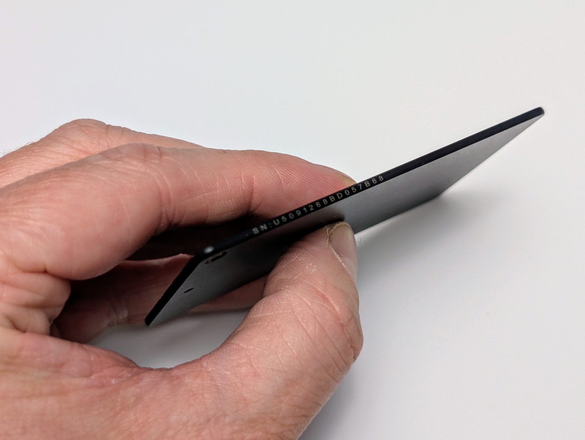 A hand holding a UGREEN FineTrack Slim Smart Finder at an angle, showing its slim black rectangular design with a small hole on one end and a serial number printed on the side, against a white background.