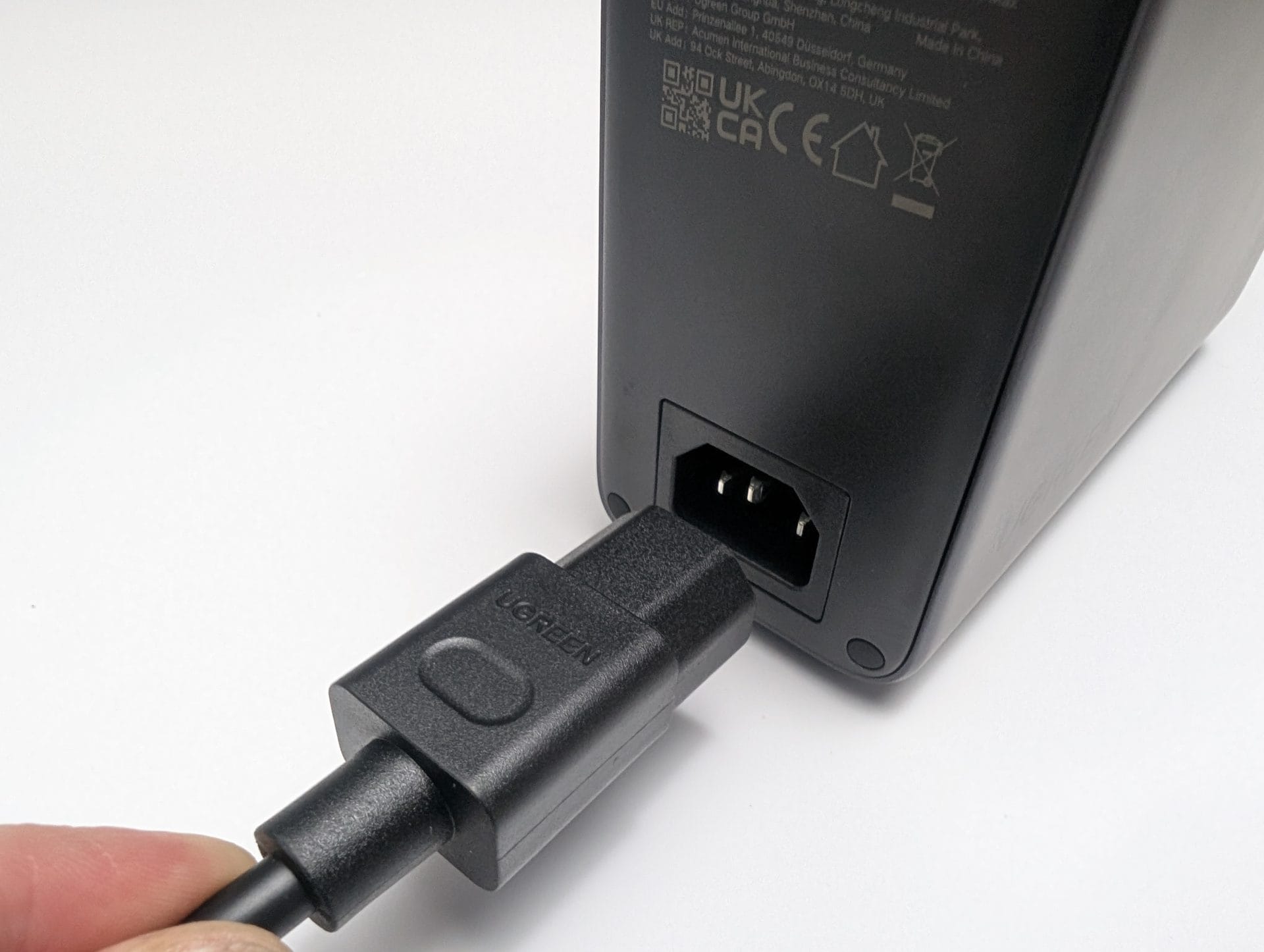 UGREEN Nexode 500W Charger The back of the UGREEN Nexode 500W 6-Port GaN Desktop Charger in grey, showing a power input port. A hand is plugging in a black power cord with a UGREEN-branded connector. Certification labels and a QR code are visible on the back, along with text indicating "EU Rep: UGREEN Group GmbH, Shenzhen, China" and "UK Rep: Acumen Int’l, 84 Oak St, Abingdon, OX14 5DH, UK". The image was captured on 31 May 2025 at 10:23 AM BST.