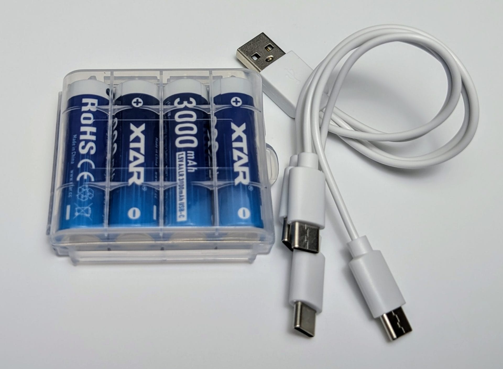 A set of four XTAR 3000mAh AA lithium batteries in a clear plastic holder, accompanied by a white USB-A to dual USB-C cable. The batteries are labeled with "XTAR," "3000mAh," and "ROHS" markings, and the cable has one USB-A connector and two USB-C connectors for charging.