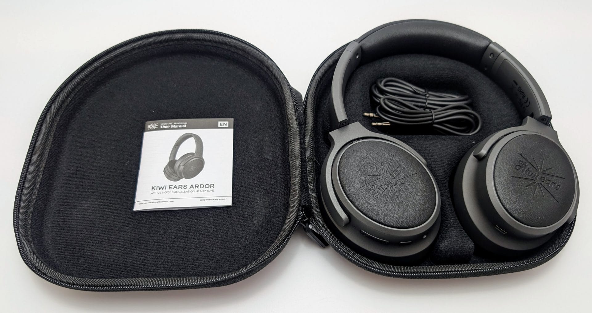 Kiwi Ears Ardor A black carrying case open to reveal a pair of Kiwi Ears Ardor headphones with active noise cancellation, featuring a gray and black design with the Kiwi Ears logo on the ear cups. Inside the case, there is a coiled audio cable and a user manual card.