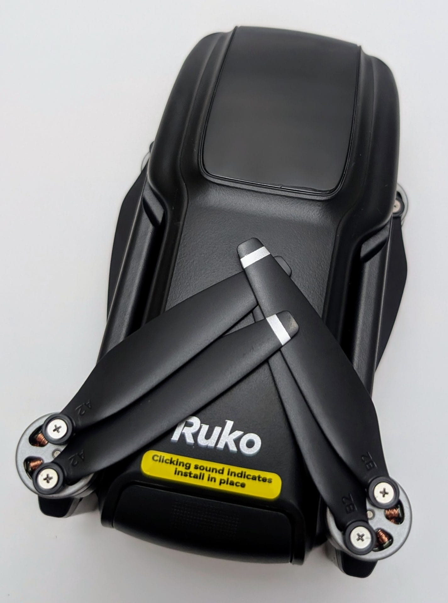 A black Ruko U11MINI 4K Drone with folded propellers, viewed from above on a white background. The drone features the "Ruko" logo and a yellow label stating "Clicking sound indicates install in place" on the body.