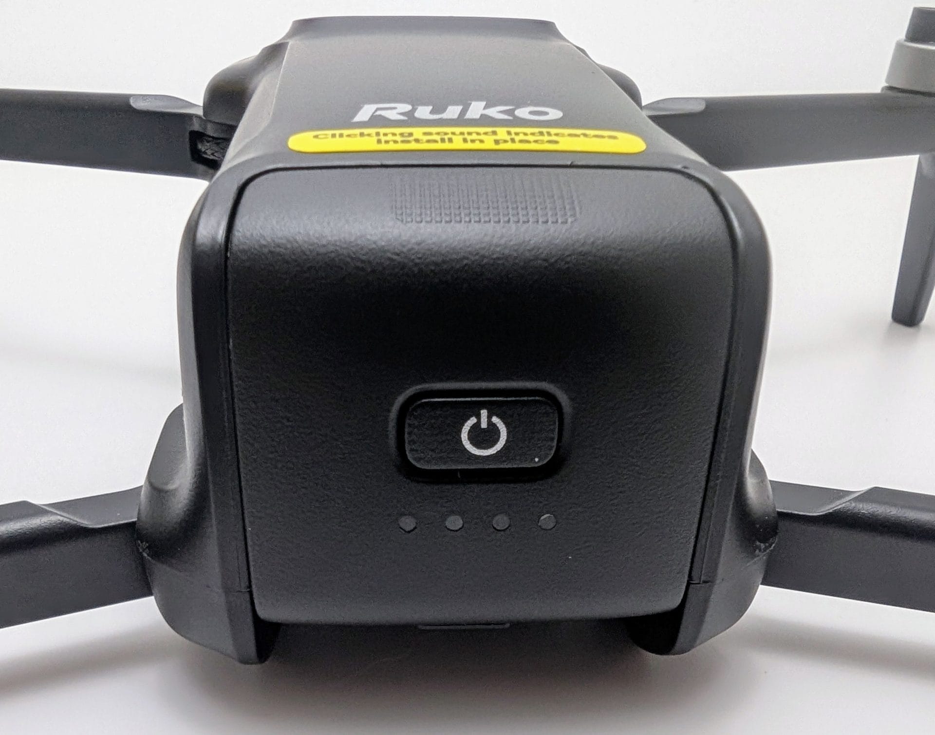 Ruko U11MINI 4K Drone A close-up view of the front of a black Ruko U11MINI 4K Drone, showing the power button and three small indicator lights below it. The drone has the "Ruko" logo and a yellow label stating "Clicking sound indicates install in place" on the body, with folded arms visible on either side.