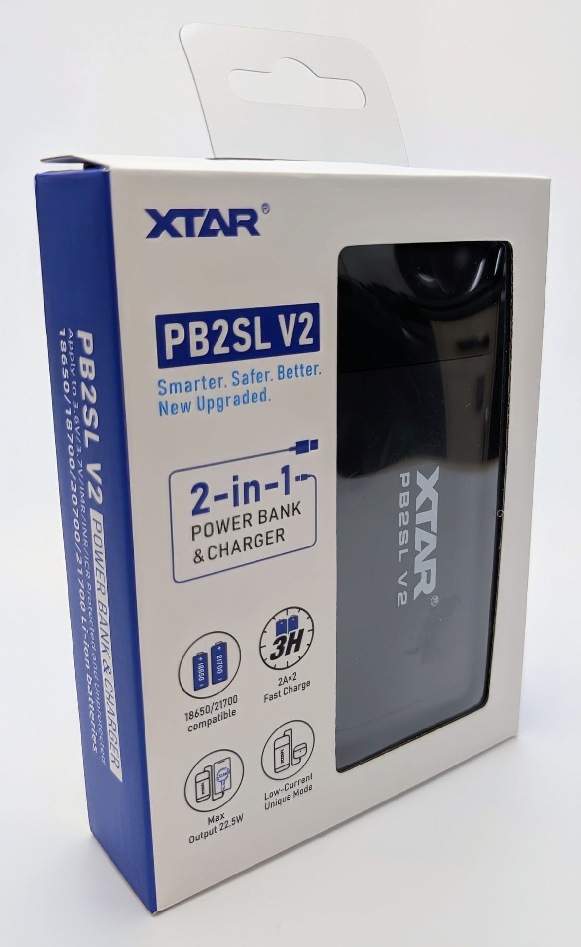 XTAR PB2SL V2 Alt text: Boxed XTAR PB2SL V2 power bank and charger, featuring a sleek black design with a transparent front panel. The packaging highlights its 2-in-1 functionality, 3-hour charging, 2A/2 fast charging, compatibility with 18650/21700 batteries, and a max output of 22W. The box includes a hang tag and detailed specs on the side.