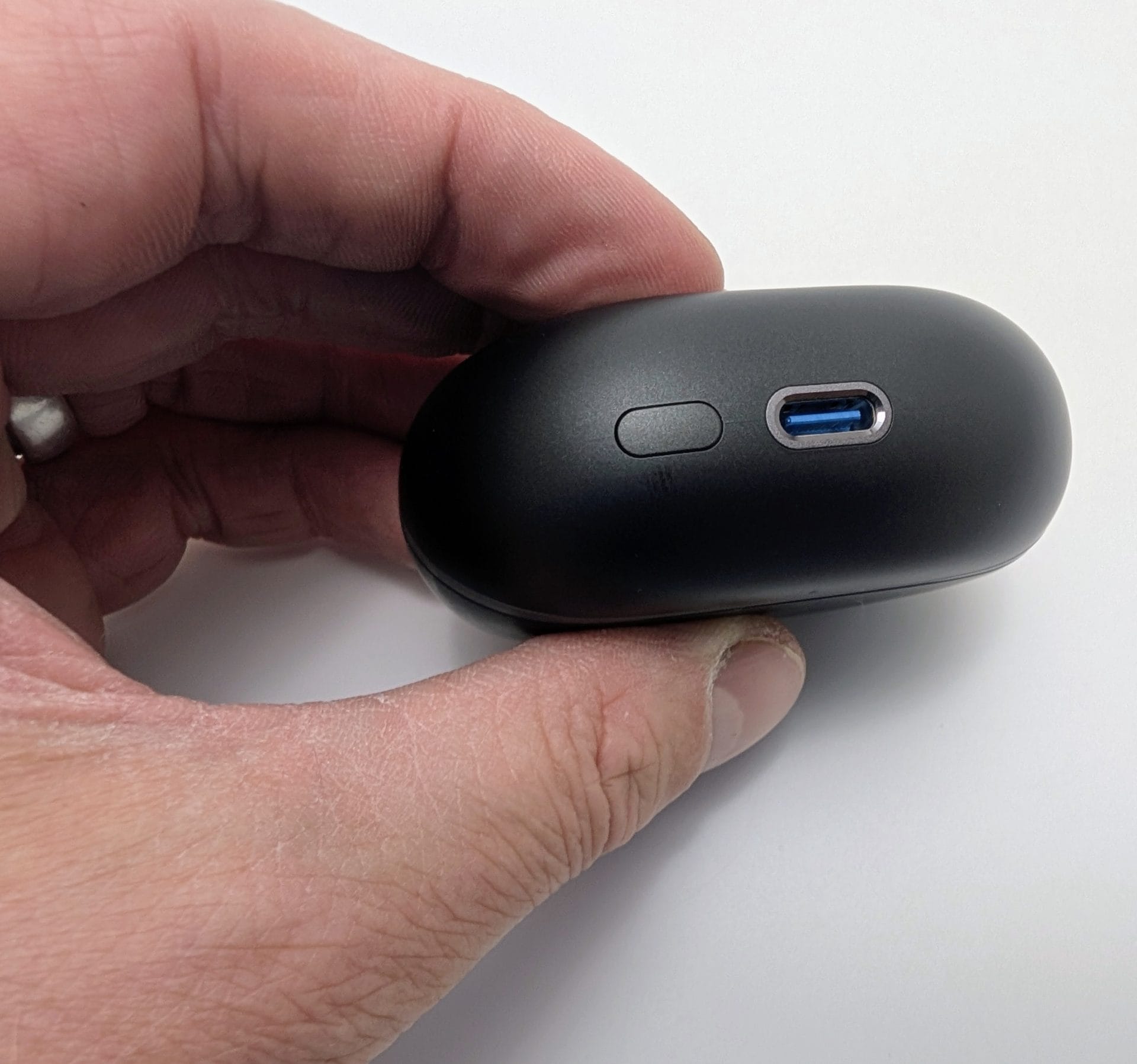 Alt text: Image of a hand holding a closed black SoundPEATS Air5 Pro earbuds charging case, showing a USB-C port and a small button on the front. The background is a plain white surface, and the hand features a silver ring.